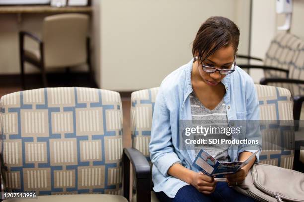 female patient reads brochure in er waiting room - blank pamphlet stock pictures, royalty-free photos & images