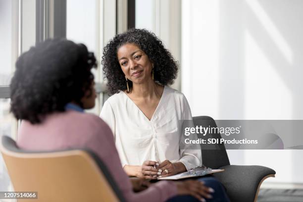 una consejera madura escucha compasivamente a una cliente femenina irreconocible - consolando fotografías e imágenes de stock