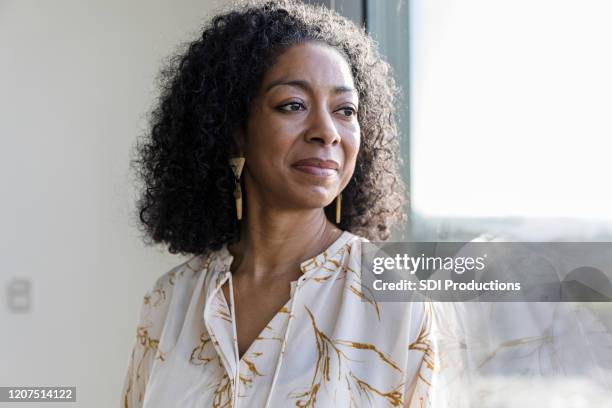 serene mature woman daydreams while looking out window - concentration curl stock pictures, royalty-free photos & images