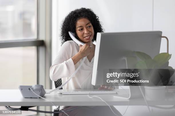 mature female professor speaks with colleagues while typing on keyboard - landline phone imagens e fotografias de stock