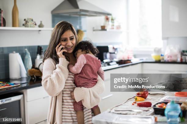 mother holding baby and multi-tasking in kitchen - baby smartphone stock pictures, royalty-free photos & images