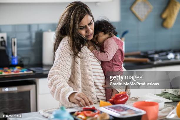mother holding baby and multi-tasking in kitchen - stay at home mother stockfoto's en -beelden