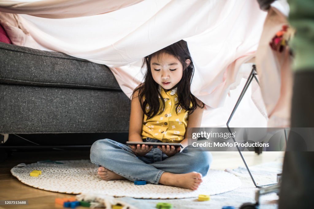 Young girl using tablet in homemade fort at home