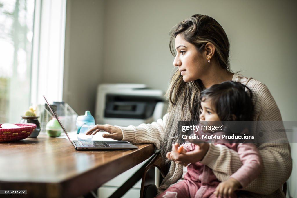 Mother multi-tasking with infant daughter in home office
