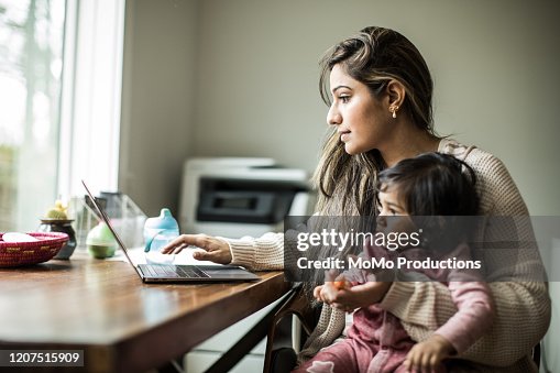 Mother multi-tasking with infant daughter in home office Mother multi-tasking with infant daughter in home office