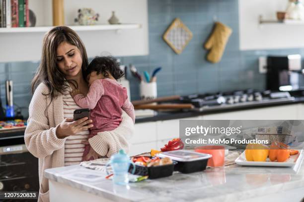 mother holding baby and multi-tasking in kitchen - text messaging mother stock pictures, royalty-free photos & images