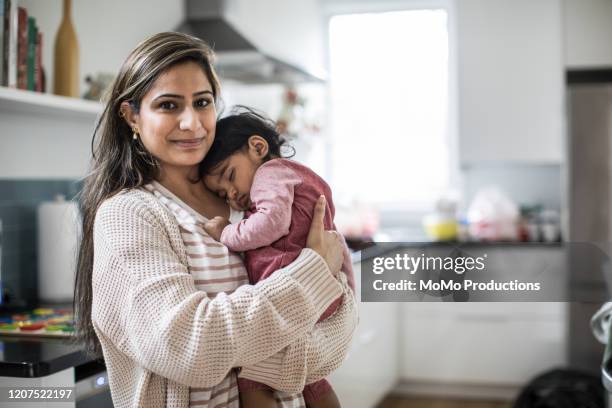 portrait of mother holding sleeping baby in kitchen - één ouder stockfoto's en -beelden