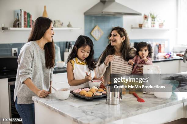 2 mothers with children makings cupcakes in kitchen - oriental asiático e indio fotografías e imágenes de stock