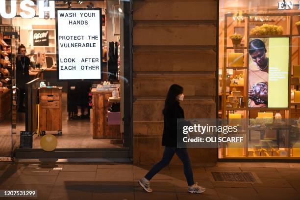 Woman wearing a protective face mask walks past a sign in a window encouraging people to wash their hands, in central Manchester on March 17 as...