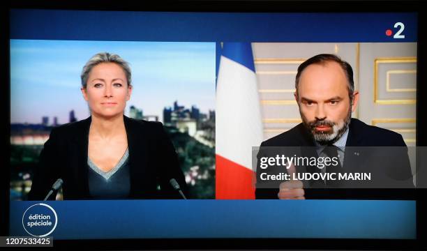 French Prime Minister Edouard Philippe is seen as he speaks from his office, next to French journalist Anne-Sophie Lapix in a studio, on a TV screen,...