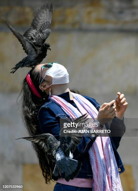 Woman uses a face mask as a precautionary measure against the spread of the new coronavirus, COVID-19, while playing with pigeons at Bolivar square,...