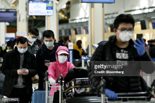 Travelers wearing protective masks wait in line in the international departures area in Vancouver International Aiport in Vancouver, British...