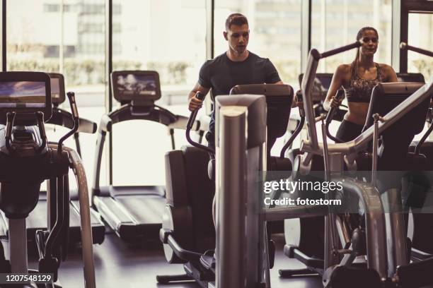 athletischer mann und frau mit ellipsentrainer im fitnessstudio - cross trainer stock-fotos und bilder