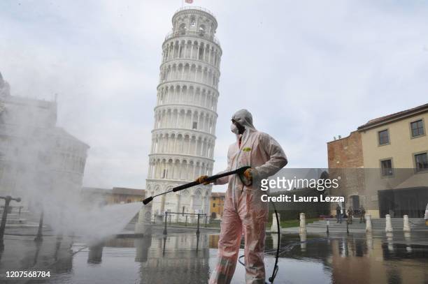 Worker carries out sanitation operations for the Coronavirus emergency in Piazza dei Miracoli near to the Tower of Pisa in a deserted town on March...