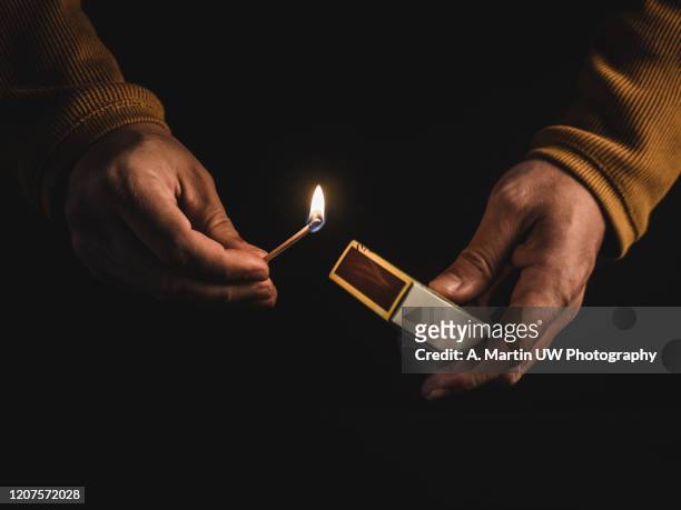 the hands of an adult man holding a burning match on black background - candela attrezzatura per illuminazione foto e immagini stock