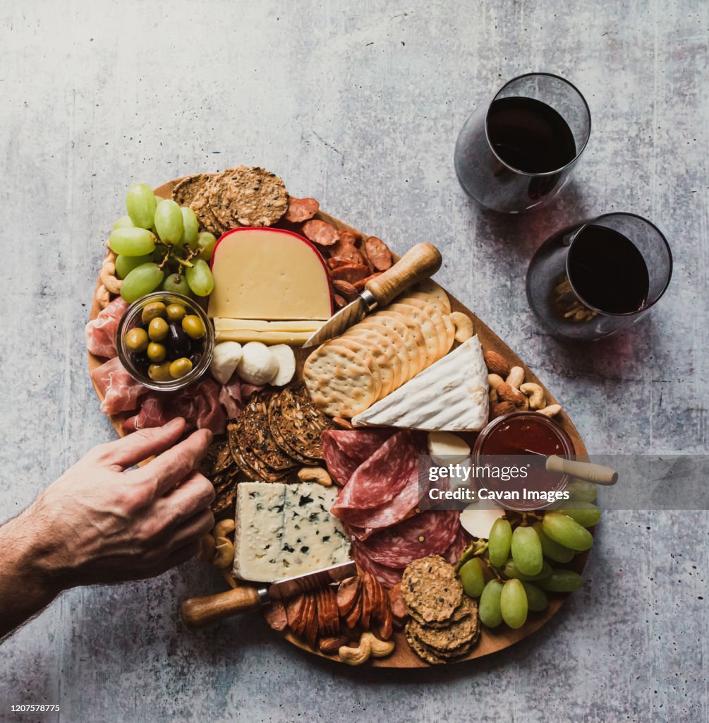 Top view of hand taking food off charcuterie board on stone counter.