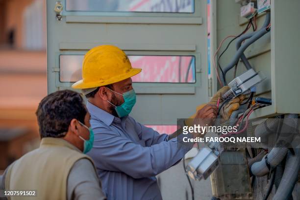Electricity workers wearing facemasks amid concerns over the spread of the COVID-19 novel coronavirus install electricity meters at a building in...