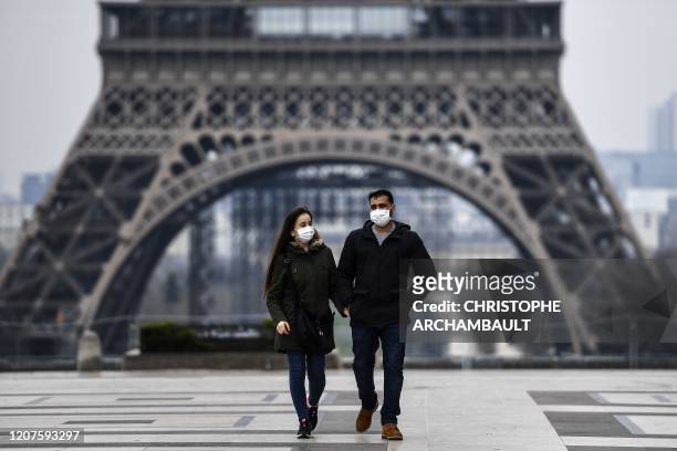 Couple wearing protective mask walks by the Esplanade du Trocadero square near the Eiffel Tower in Paris, on March 18 a day after a strict lockdown...