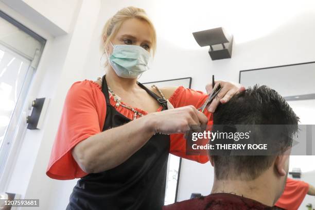 Hairdresser wearing a facemask for protective measures as she cuts the hair of a client in Brussels, on March 18, 2020 as a strict lockdown came into...