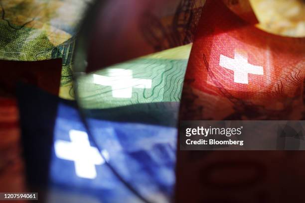 The cross of the Swiss national flag sits on Swiss franc banknotes in an arranged photograph in Bern, Switzerland, on Saturday, March 14, 2020....