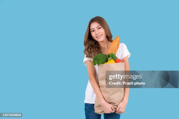 beautiful smiling asian woman holding paper shopping bag full of fresh vegetables and groceries and smiling, studio shot isolated on cyan background. carrying a healthy bag. - food studio shot stock pictures, royalty-free photos & images