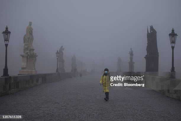 Solitary pedestrian wearing a protective face mask crosses the Charles Bridge at dawn in Prague, Czech Republic, on Wednesday, March 18, 2020. The...