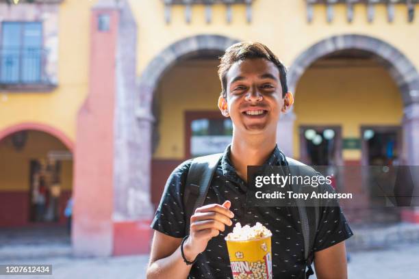 young man eating popcorn in town square - handsome mexican men - fotografias e filmes do acervo