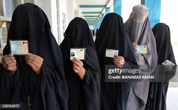 Burqa-clad Afghan women show identification cards as they wait to cast their votes at a school converted to a polling centre in Kandahar on August...