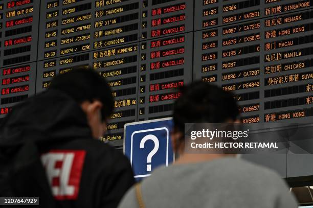 Couple wearing face masks, amid concerns of the COVID-19 coronavirus, look at a screen showing international departures at Shanghai Pudong...