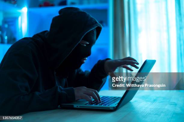 dangerous hooded hacker breaks into government data servers and infects their system with a virus. his hideout place has dark atmosphere - ransomware stock pictures, royalty-free photos & images