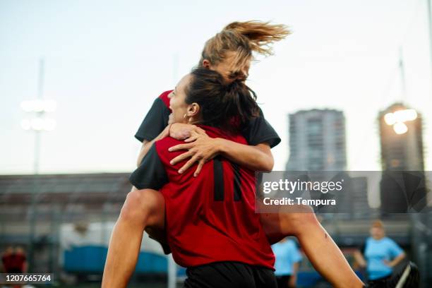 two woman soccer team mates hug after scoring a goal in celebration. - women soccer goal stock pictures, royalty-free photos & images