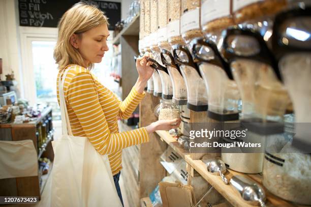woman in whole foods refill store dispensing oats into jar. - bioladen stock-fotos und bilder