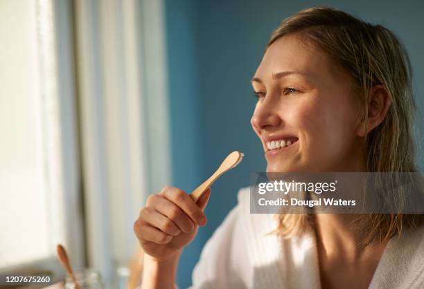 happy woman in bathrobe brushing teeth with plastic free toothbrush. - toothbrush stock pictures, royalty-free photos & images