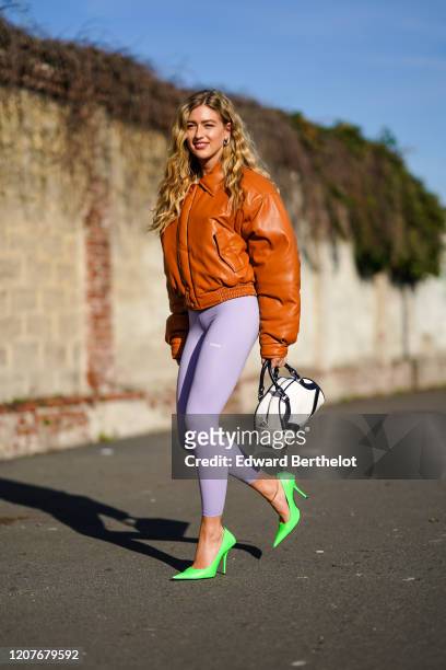 Emili Sindlev wears a brown/orange leather bomber jacket, a white bag, pale purple leggings, green pointy shoes, outside Prada, during Milan Fashion...