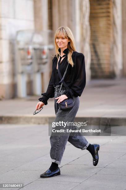 Jeanette Madsen wears a black shirt, a Saint Laurent YSL bag, gray denim large pants, black leather shoes, black socks, outside Vivetta, during Milan...