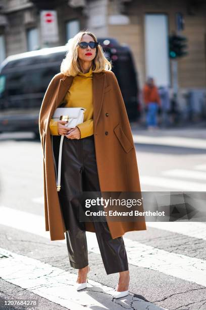 Candela Novembre wears an orange pullover, a white bag, a brown long coat, black leather pants, white pointy shoes, outside Max Mara, during Milan...