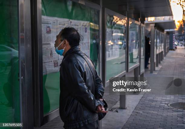 Chinese man wears a protective mask on his chin while reading a Communist Party newspaper outside on March 19, 2020 in Beijing, China. With the...