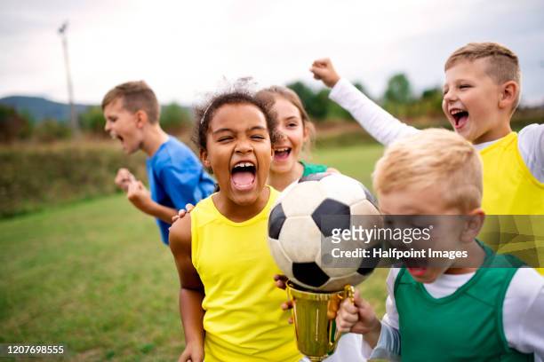 a group of children with cup prize standing outdoors on football pitch. - sportbegriff stock-fotos und bilder