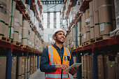 Low angle view of young african man wearing reflective jacket holding digital tablet standing in factory warehouse smiling