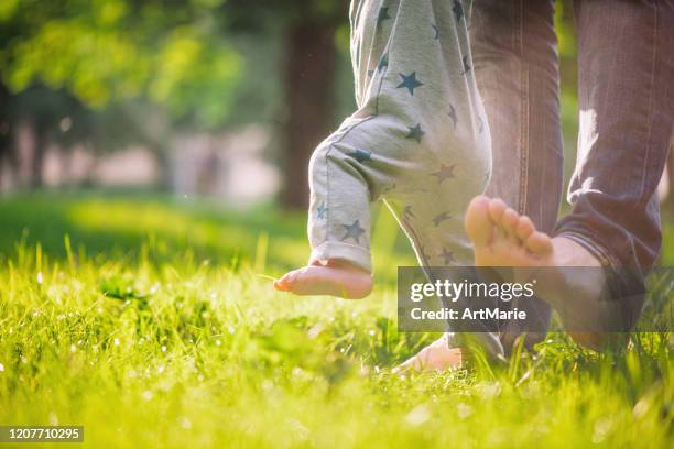 baby boy is happy with his first steps supported by his father on a summer meadow - descalço imagens e fotografias de stock