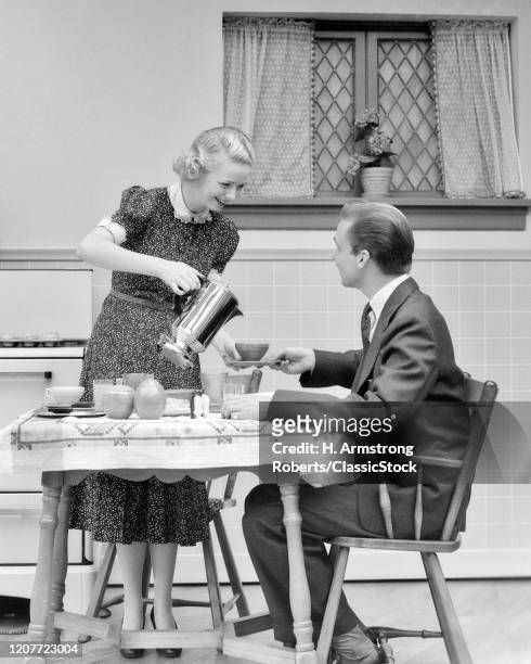 1930s couple in kitchen man seated at table woman pouring him a cup of coffee.