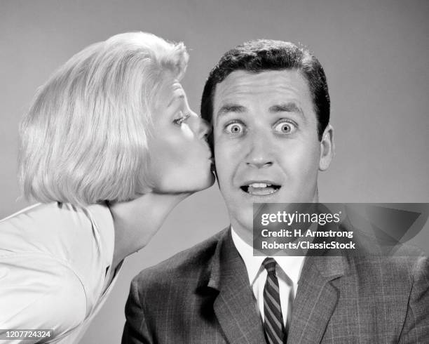 1960s blonde woman kissing surprised bug-eyed wide-eyed man on cheek .