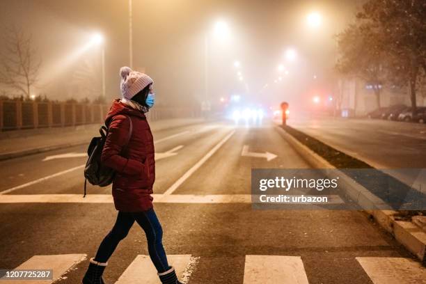 frau mit maske überqueren straße - pollution masks stock-fotos und bilder