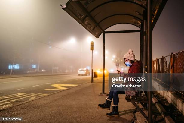 woman with mask using phone on bus stop - smog city stock pictures, royalty-free photos & images