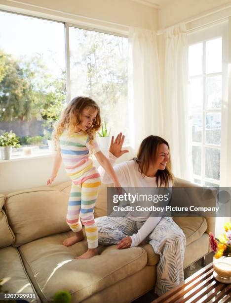 adorable niña bailando en pijama en un sofá con su madre riendo - chica bailando en pijama fotografías e imágenes de stock