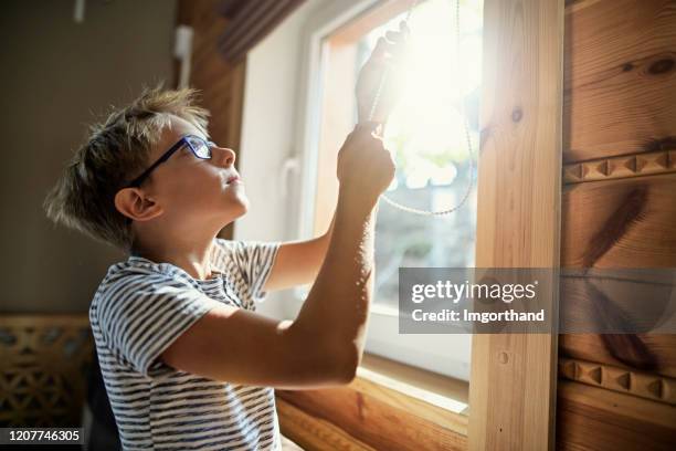 niño pequeño cerrando las persianas enrollables en el día caliente para ahorrar energía de aire acondicionado - persiana fotografías e imágenes de stock