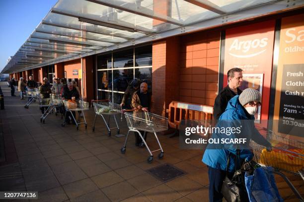 Shoppers queue before the 7am opening time to enter a Sainsbury's supermarket in Oldham, northern England, on March 20, 2020. - The British prime...