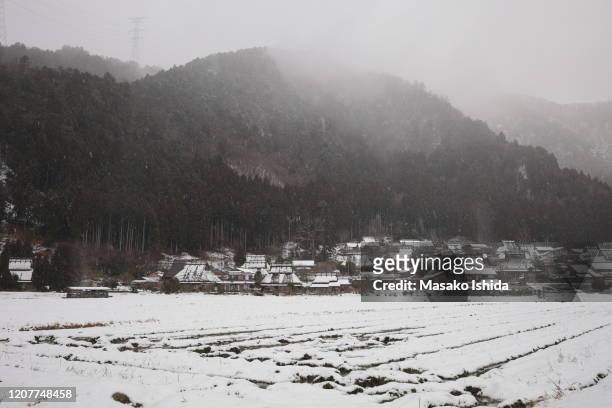 tranquil winter landscape with snow covered traditional japanese thatched roof houses and farm field in a snowy day.fog lies over the mountains covered with cedar trees. miyama kayabuki-no-sato village ,kyoto prefecture,japan. - kyoto covered with first snow of the season imagens e fotografias de stock