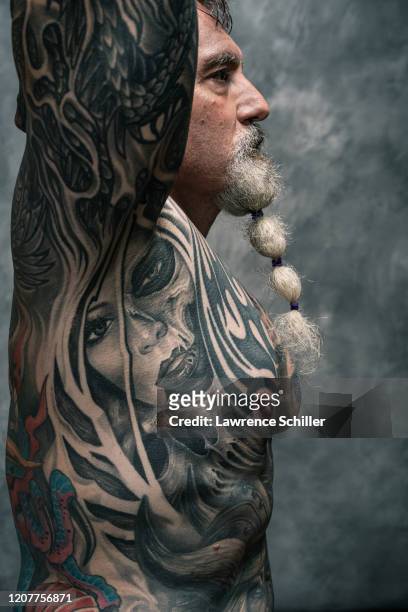 Portrait of retired executive Charles Venancio as he shows the tattoos on his arms, chest, and torso, New York, New York, June 20, 2019. He wears leg...