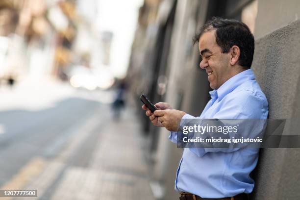 korte mens die slimme telefoon gebruikt terwijl het leunen op een muur - dwarf stockfoto's en -beelden